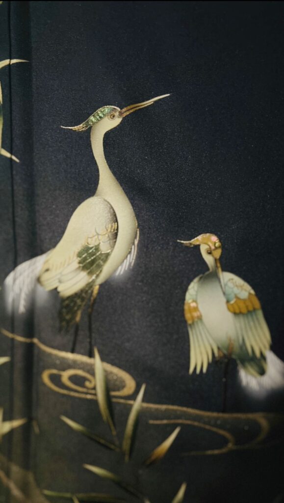藍色の訪問着の柄アップ。水辺に立つ鷺(さぎ)の意匠と金彩の表現