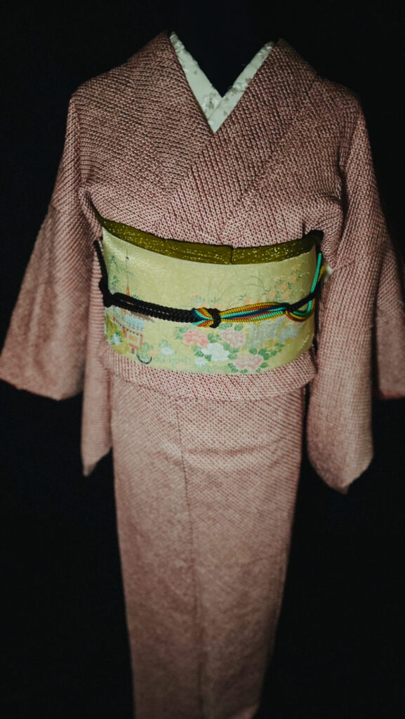 袋帯の柄アップ（建物の意匠と草花文様、黒の帯締めが横に走る）