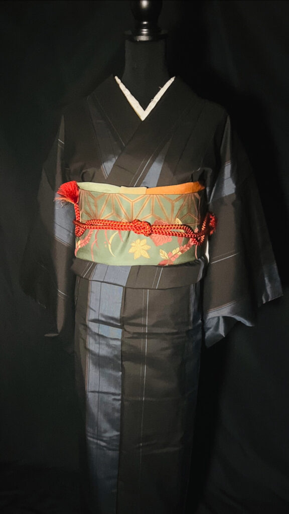 黒の大島紬（単衣）に緑系の柄帯、赤の帯締めを合わせたコーディネート（家紋なし）