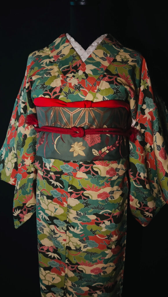 小紋の柄アップ（多色の草花と葉文様）。黒を基調にした地色に配色が映える