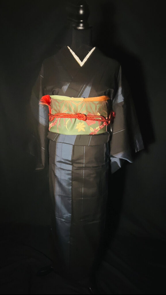 黒の大島紬（単衣）の全身。黒地の陰影と帯の緑・赤の配色バランスがわかる写真（家紋なし）