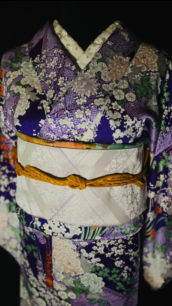 紫地に菊や小花の文様が重なる袷の正絹小紋の衿元アップ。草花柄の半衿と帯上の配色が分かる近景(家紋なし)