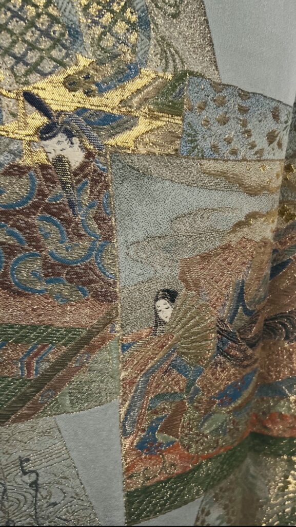 百人一首の意匠が描かれた訪問着の裾アップ。人物と短冊、金彩が重なる情景文様の細部（袷・家紋なし）