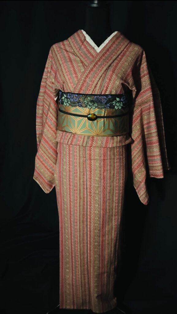 赤茶の縞模様のウール着物を着付けた全身写真。緑×金の幾何学柄の帯がポイント（家紋なし）