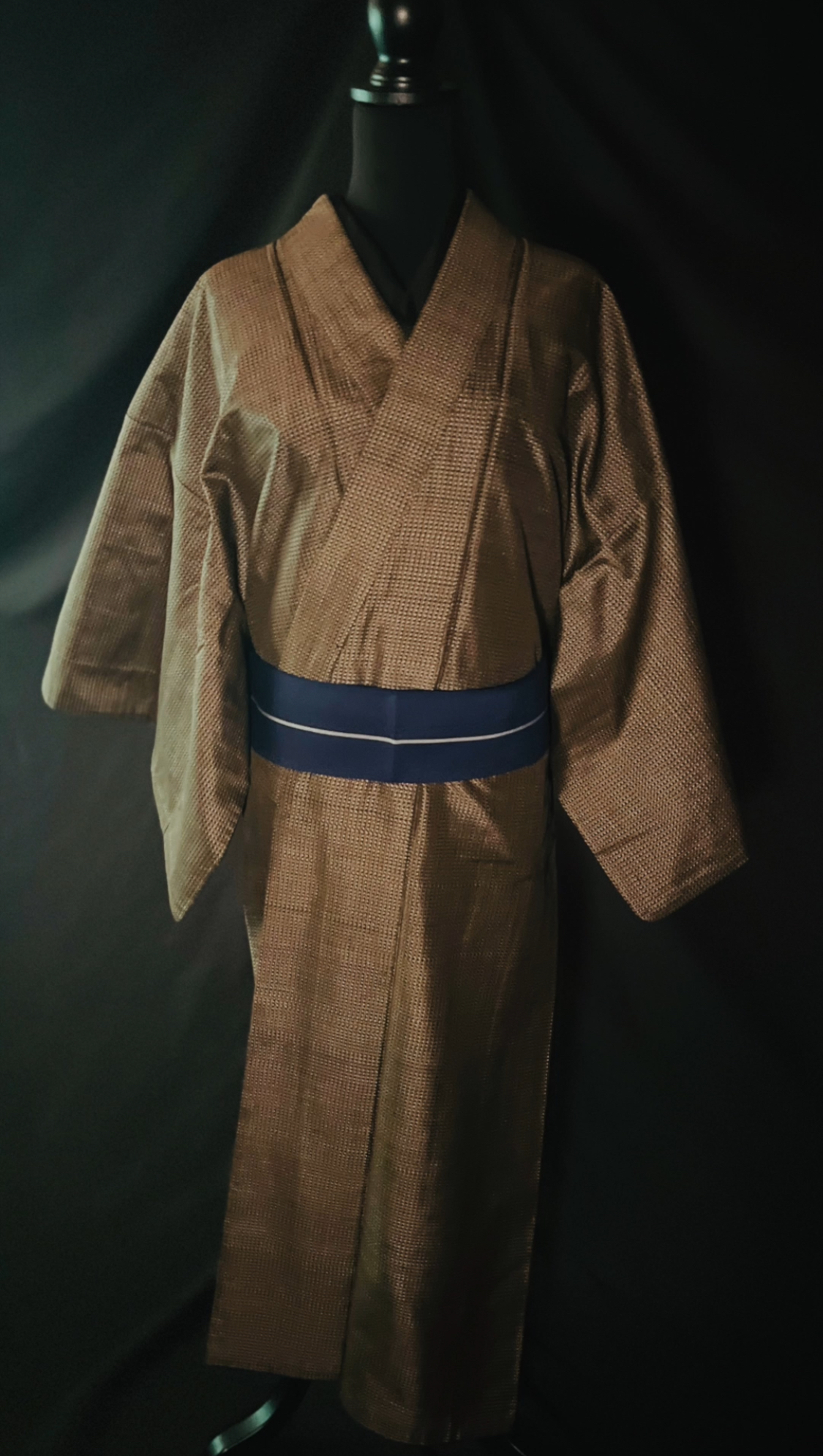 茶系の男仕立ての大島紬に青の帯を合わせた着姿