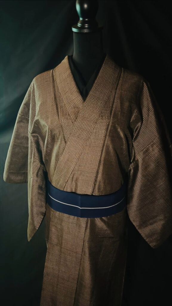 茶系の大島紬と青帯のコントラストが分かる着姿