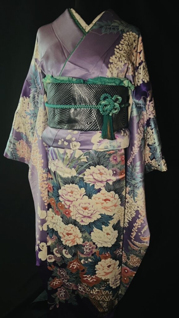 Vintage purple furisode kimono with floral patterns and a dark obi accented with green cord, photographed against a black background.