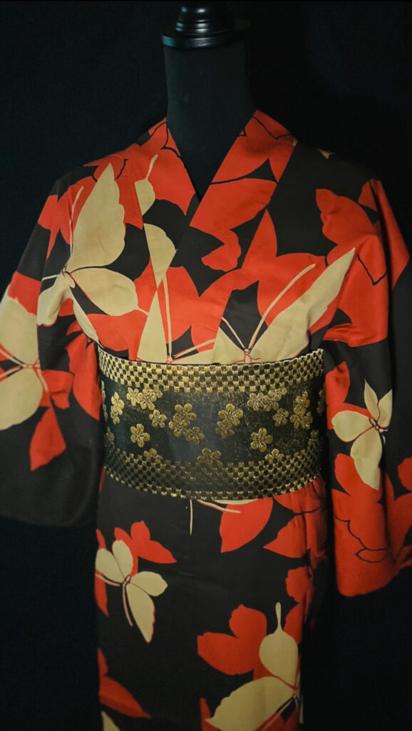 黒地にオレンジの花と黄色の蝶が描かれた浴衣の上半身。金糸が光る黒い半幅帯を合わせた装い