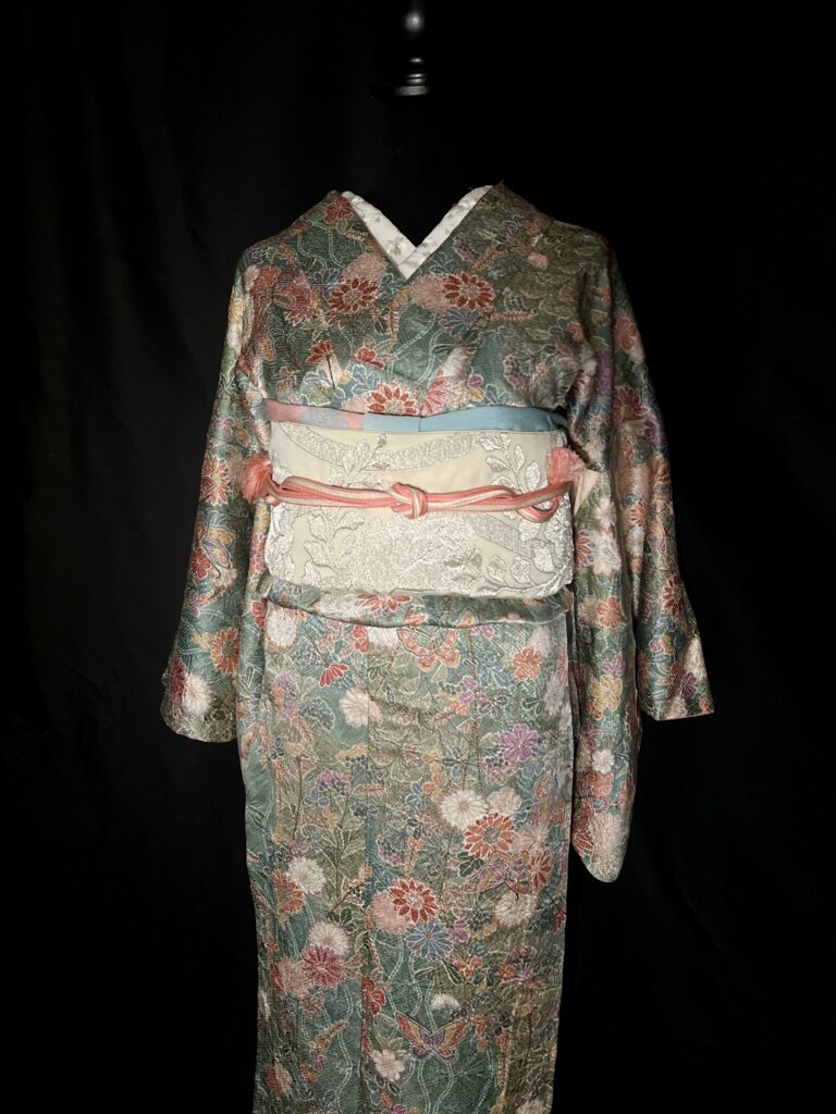 花と蝶を描いた緑色の正絹小紋に淡い袋帯と水色や桃色の小物を合わせた着姿