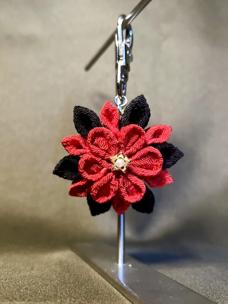 鮮やかな赤と黒の花びらを重ね、中央にパール調の飾りをあしらったatelier aloの立体的なつまみ細工バッグチャーム。