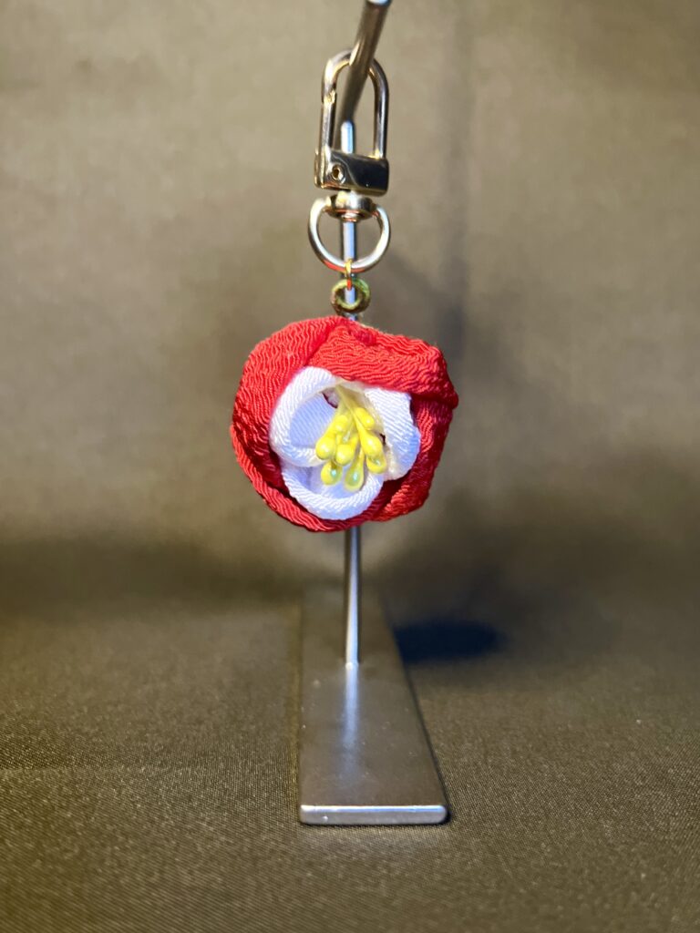 赤と白の布を重ね黄色の花芯を添えたatelier aloの椿モチーフつまみ細工バッグチャーム。